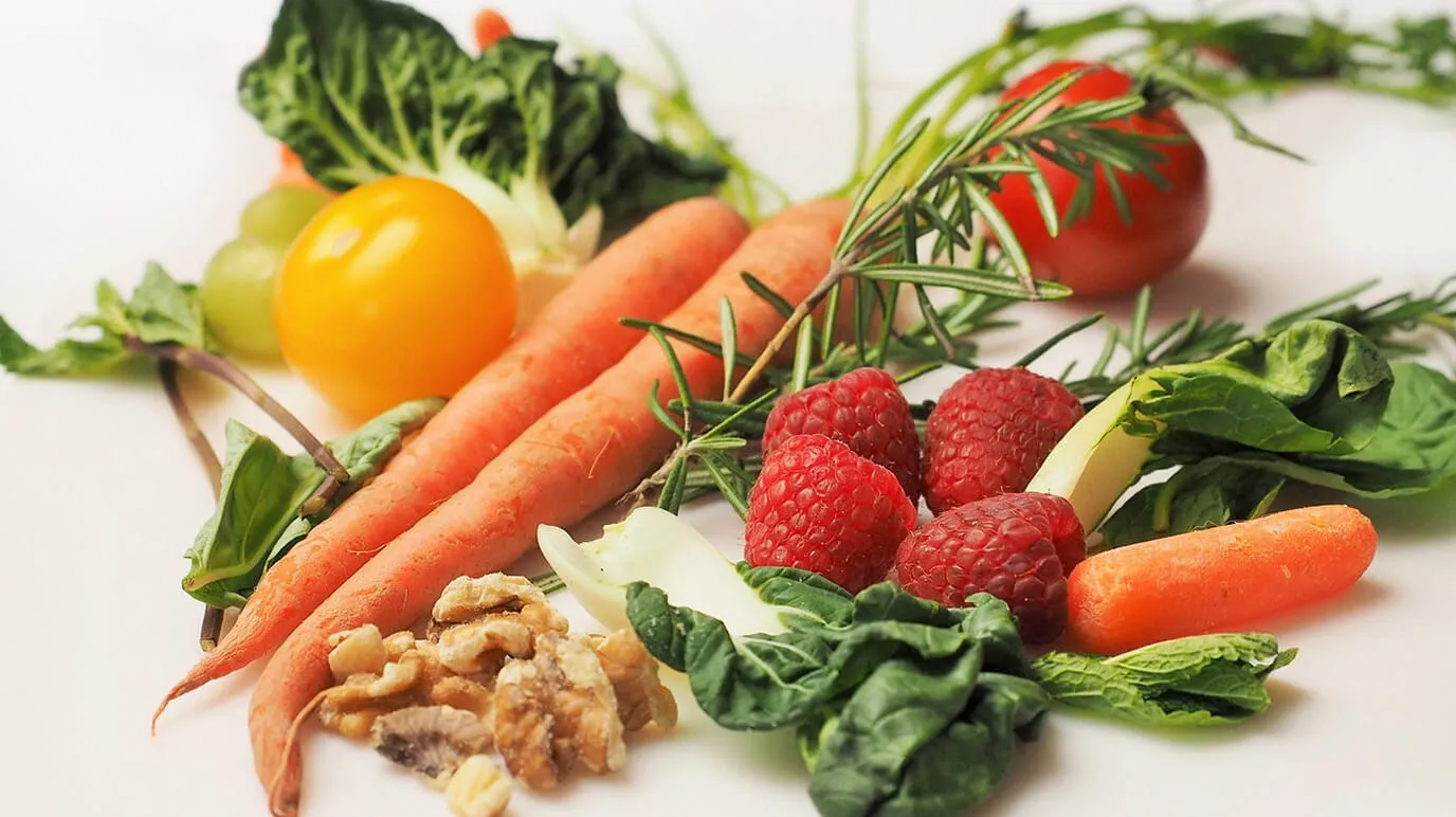 Fresh vegetables, fruit, berries and nuts on a table, comparing low-calorie and high-calorie foods